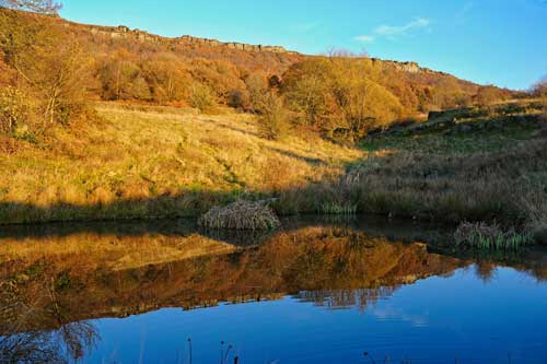 Autumn colours and a Peak District gritstone edge reflected in a still pond