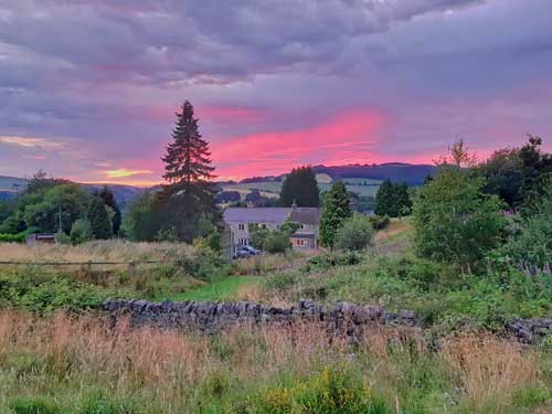 A pink sunset over a stone cottage and drystone wall in the Peak District